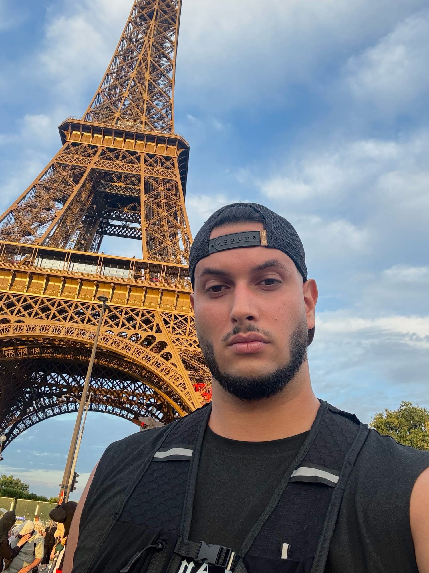 Selfie in a backwards cap and black running vest below the Eiffel Tower.