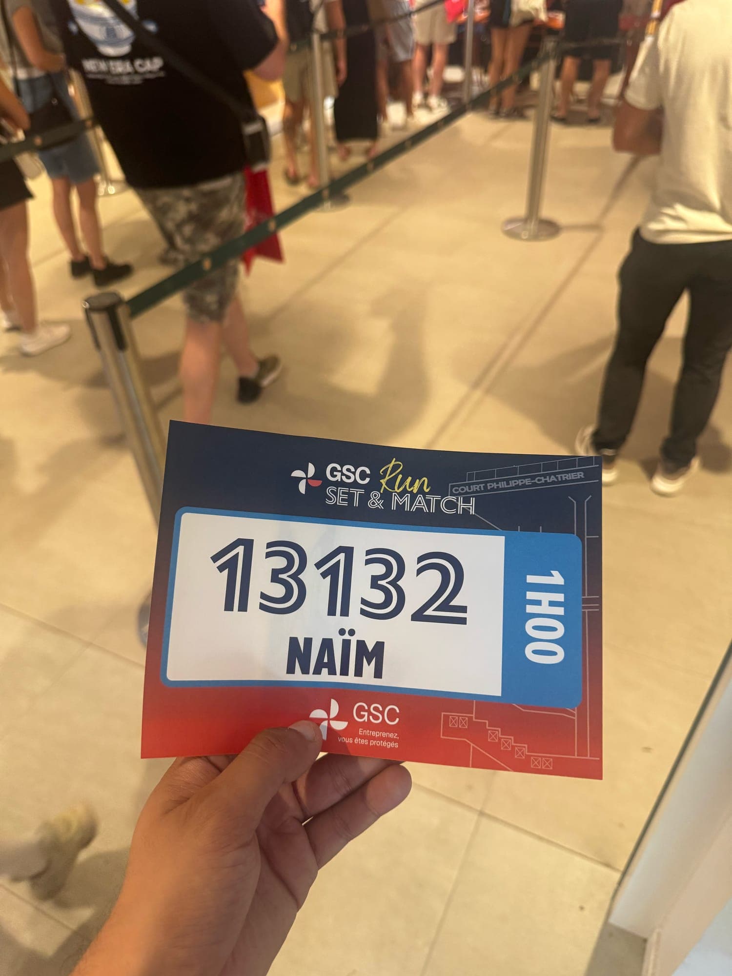 Hand holding a race bib reading GSC Run Set & Match, Court Philippe-Chatrier, 1H00, number 13132 and the name Naïm.