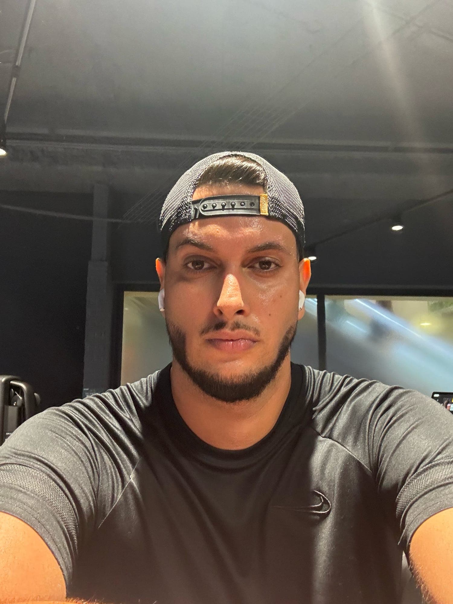 Selfie indoors in a fitted grey long-sleeve top and backwards cap.